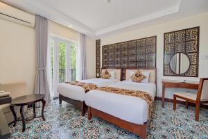 a bedroom with two beds and a table and a desk at Hoi An Canal House Riverside By Haviland in Hoi An
