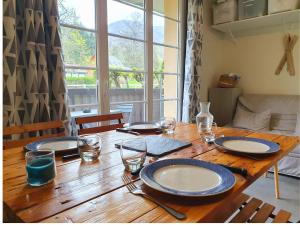 a wooden table with plates and glasses on it at La Pause Bourboulienne Appartement RDC avec balcon in La Bourboule