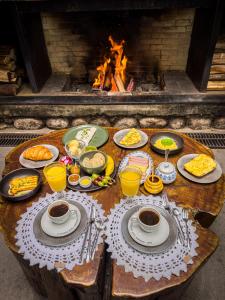a table with plates of food and drinks and a fireplace at Hotel Giardino Di Pietra in Gramado