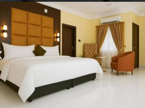 a bedroom with a large white bed and a chair at Darminah Hotel in Akure