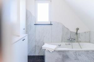 ein weißes Badezimmer mit Badewanne und Fenster in der Unterkunft Villa Croisette in Nieuwpoort