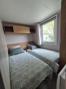 deux lits dans une petite pièce avec une fenêtre dans l'établissement MOBIL HOME BISCAROSSE LAC - Loc du Samedi au Samedi uniquement, à Biscarrosse