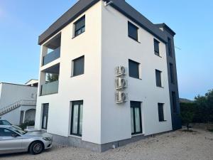 un bâtiment blanc avec une voiture garée devant dans l'établissement Apartmani VIR, à Vir