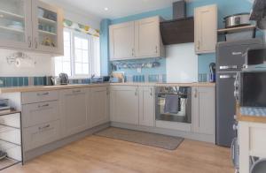 a kitchen with white cabinets and blue walls at Inner Harbour Cottage in Portreath