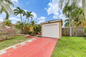 a garage on a red driveway in a yard with palm trees at Golf and Shop Gem with Private Pool in Boca Raton in Boca Raton