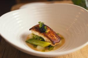 a white plate with a piece of fish and vegetables at Stoke Lodge Hotel in Stoke Fleming