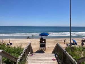 a beach with a blue umbrella and people on the beach at Downtown Duck Resort Perks Ocean Views & Hot Tub in Duck