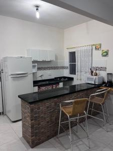a kitchen with a counter and two chairs and a refrigerator at LINDO SOBRADO PERTINHO DA PRAIA - WiFi 600 MEGAS in Bertioga
