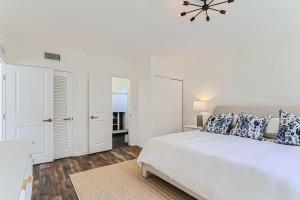 a white bedroom with a large bed and a chandelier at The Glenn House - Gather Poolside in a Breezy South End Getaway in West Palm Beach