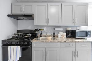 cocina con armarios blancos, fogones y fregadero en Peaceful Hideaway - NYC & NWK with free parking, en Newark