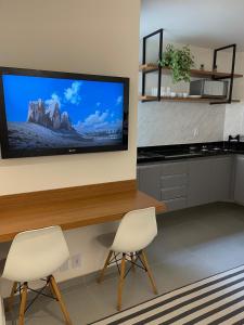 Lindo Apartamento - 600 metros da Praia de Itaparica في فيلا فيلها: مطبخ مع كرسيين وتلفزيون بشاشة مسطحة على الحائط