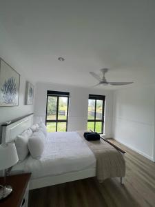 a white bedroom with a bed and two windows at Madora Bay Beach House in Singleton