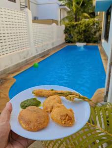 une personne tenant un plateau de nourriture à côté d'une piscine dans l'établissement Solace Est 6BR Family Pool Villa Candolim Cook, à Candolim