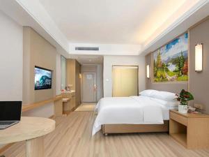 a bedroom with a bed and a desk with a laptop at Vienna Hotel Jiangxi Fengcheng Fnegkuang in Fengcheng
