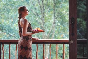 a woman standing on a balcony holding a plate of food at Harsa Sanctuary by GenuineHost in Ubud