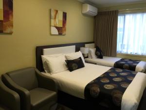 una habitación de hotel con 2 camas y una silla en Park Squire Motor Inn & Serviced Apartments, en Melbourne