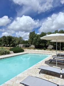 een zwembad met een parasol en 2 ligstoelen bij Trullo Tranquillo Ostuni in Ostuni