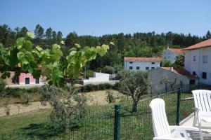 two white chairs and a fence with trees and houses at Alojamento Antonio in Castanheira de Pêra