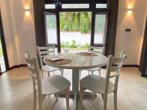 Una mesa de comedor blanca con sillas y una mesa y ventana blancas. en The Cottage Ambuluwawa, en Gampola