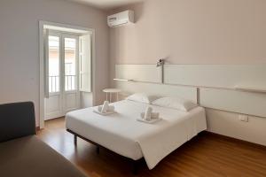 a white bedroom with a bed and a chair at Margherita Rooms in Catania
