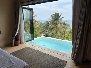 a bedroom with a large window with a swimming pool at Aether Hilltop Villas in Dickwella