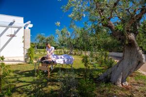 a woman sitting on a bed under a tree at Cala Ponte, a Tribute Portfolio Hotel in Polignano a Mare