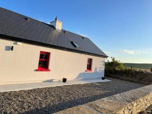un edificio bianco con finestre rosse e tetto di Dun Aengus Cottage on the Cliffs of Moher a Liscannor