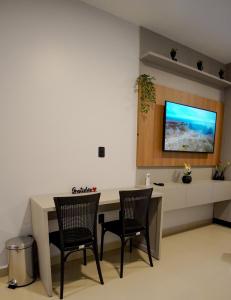 a room with a desk with two chairs and a tv on the wall at Studio no Daia- Kitnet Completa in Anápolis