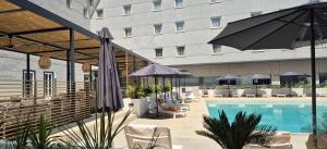 una piscina de hotel con sillas y sombrillas y un edificio en Vértice Sevilla Aljarafe, en Bormujos