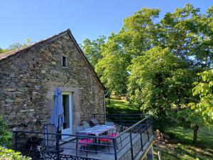 a stone house with a deck with chairs and an umbrella at Le sécadou in Montirat