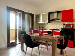une cuisine avec une table en bois, des chaises et des armoires rouges dans l'établissement La Casetta di Lally, à Cabras