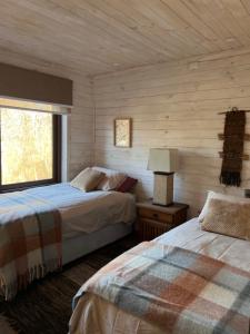two beds in a room with wooden walls and a window at Refugio Vista Sierra Nevada in Malalcahuello