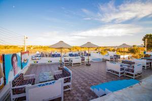 Un patio con mesas y sillas blancas y sombrillas. en Kulaih nubian guest house, en Asuán