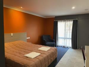 a bedroom with a large bed and a chair at Homestead Motel in Dubbo
