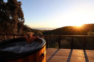 a woman sitting in a hot tub on a deck with the sunset at Foudre Suite with Hot Tub at Barrelled Wines Raglan in Raglan