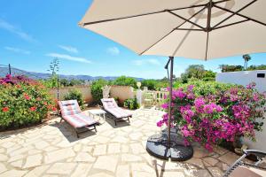 un patio con 2 sillas, sombrilla y flores en Beate - holiday bungalow with pool in Moraira, en Moraira