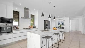 a kitchen with white cabinets and bar stools at Pura Villa - Tropical Luxury Living in Palm Cove