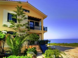 una casa amarilla con un árbol frente al océano en Villa Corali, en Karfas