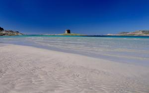 a beach with sand and the ocean with a lighthouse in the background at Villa Stintino in Stintino