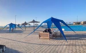 two people sitting on a bench under blue nets on the beach at On the beach house in Al Ḩammām