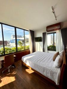 a bedroom with a bed and a desk and windows at CHAMECO ART Boutique Home Danang in Da Nang