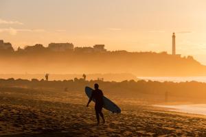 a man walking on the beach with a surfboard at Hôtel Maison Chiberta in Anglet