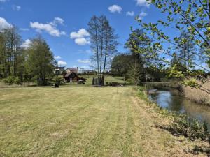 a field next to a river with a house in the background at Sodyba LAIMĖS SLĖNIS in Kapčiamiestis