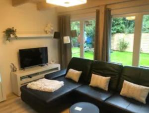 ein Wohnzimmer mit einem schwarzen Ledersofa und einem TV in der Unterkunft Luxus Summer Breeze Ferienhaus Lübbesee Sauna Bootssteg Templin in Milmersdorf