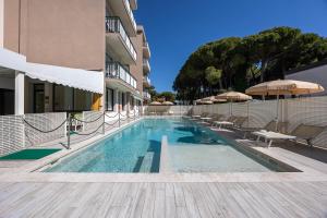 a swimming pool with chairs and umbrellas next to a building at Hotel Picobello Pineta in Lido di Jesolo