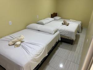 Dos camas con sábanas blancas y zapatos en una habitación. en May acomodações, en Barreirinhas
