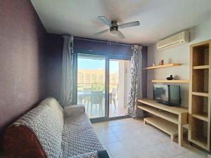 ein Wohnzimmer mit einem Sofa, einem TV und einem Balkon in der Unterkunft Ayf 200m del mar 2 piscinas, pista de padel y gym in Oropesa del Mar
