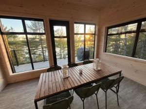 a wooden table and chairs in a room with windows at Chalet Cottage Le Bellevarde Hot tub Lake view in Saint-Aimé-Du-Lac-des-Îles