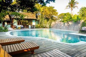 a swimming pool with a wooden deck and a house at Vila Botanika Caraíva in Caraíva