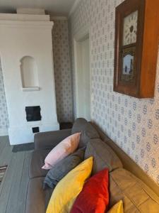 a couch with colorful pillows in a living room with a clock at SwedishCountryLiving / Skippers cottage in Köpmannebro +18 photos